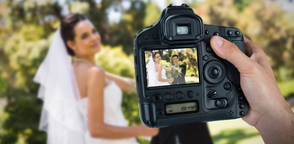 Cropped Hand Holding Camera Against Happy Newlywed Couple with Bouquet